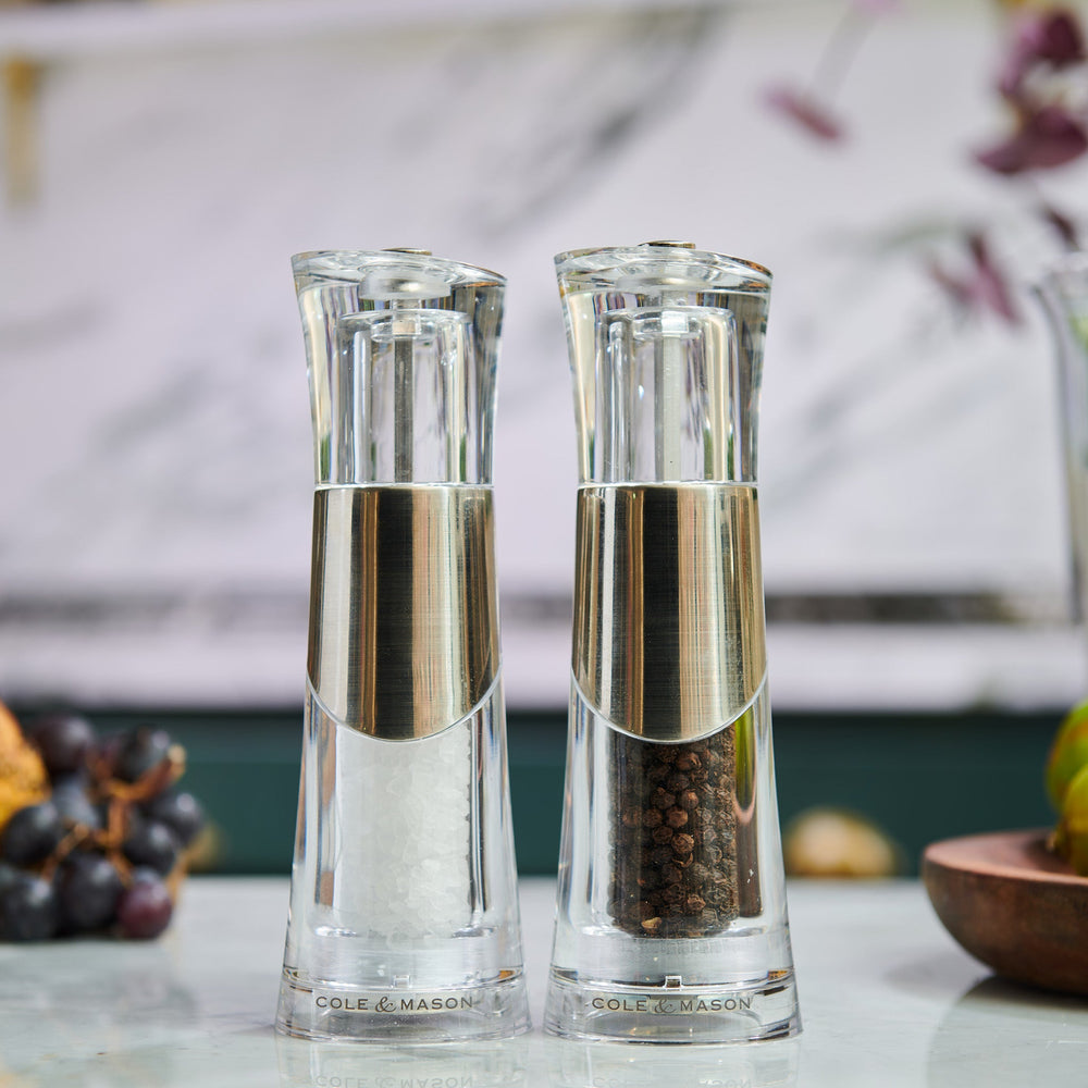 The Cole & Mason Bobbi Salt & Pepper Mill Set features two clear, modern mills with silver accents, adjustable grinders, and durable mechanisms. Each is prefilled with black peppercorns or coarse sea salt and labeled Cole & Mason at the base.