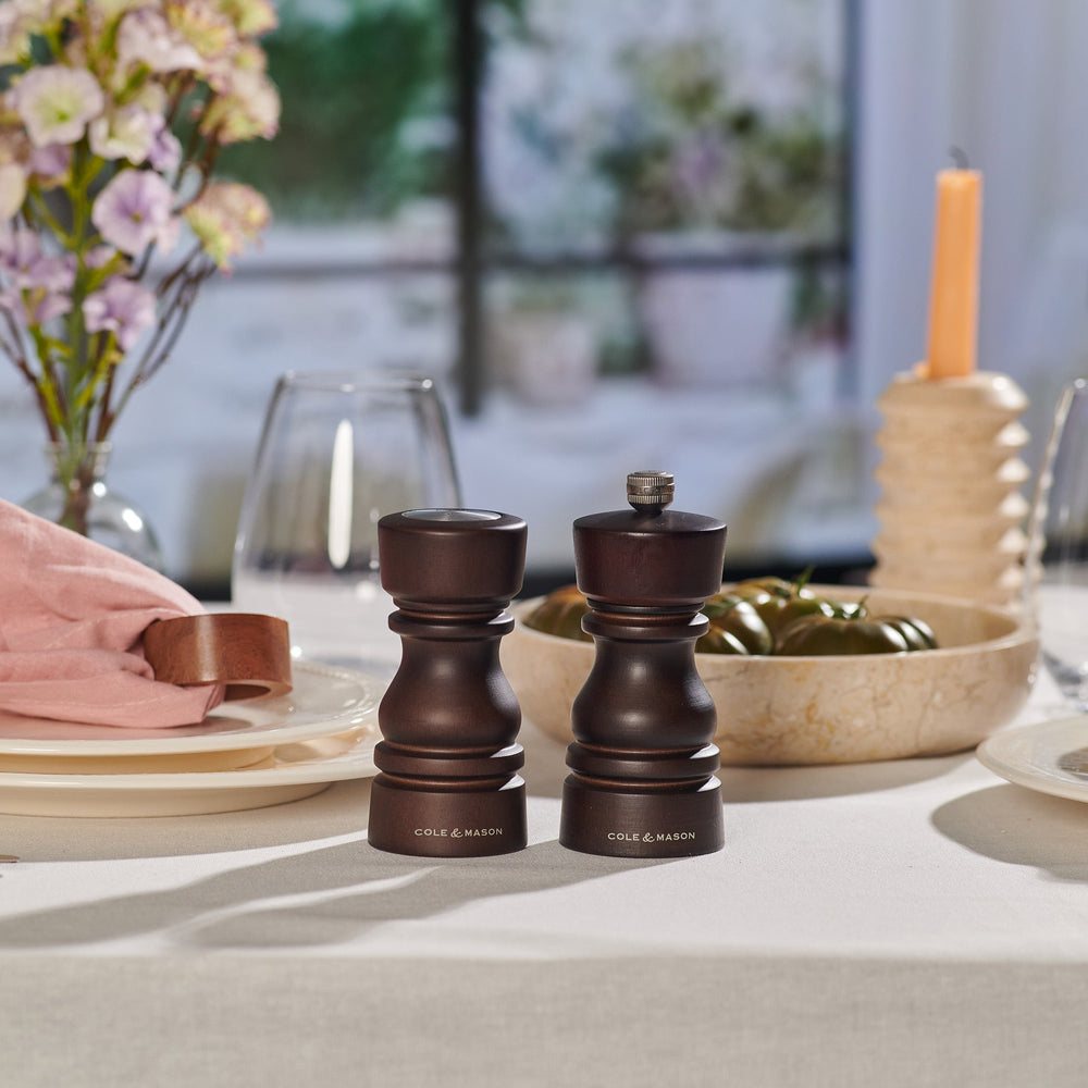 The Cole & Mason London Chocolate Wood Salt Shaker & Pepper Mill Set features two dark wood mills: the pepper mill with grind select technology and a knob, and the shorter, knob-less salt shaker with a premium grinding mechanism.