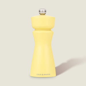 The Cole & Mason Kenton Salt & Pepper Mill in Turmeric Yellow features a silver top knob, brand logo at the base, and a durable ceramic grinding mechanism. Its photographed on a plain light background with a soft shadow to the right.