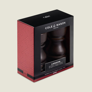 The Cole & Mason London Chocolate Wood Salt Shaker & Pepper Mill Set features premium grinding mechanisms and natural wood, presented in elegant black and red packaging with a clear display window.