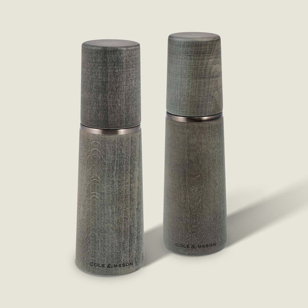 Two Marlow Grey Beech Salt & Pepper Mills by Cole & Mason UK, featuring a smooth tapered shape and wood grain, stand upright on a light background with an adjustable grinding mechanism for custom seasoning.